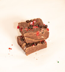 Two pieces of chocolate peppermint fudge stacked on soft white background