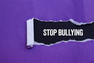 Stop bullying message written on ripped torn purple paper on black background. Conceptual stop bullying symbol. Copy space.