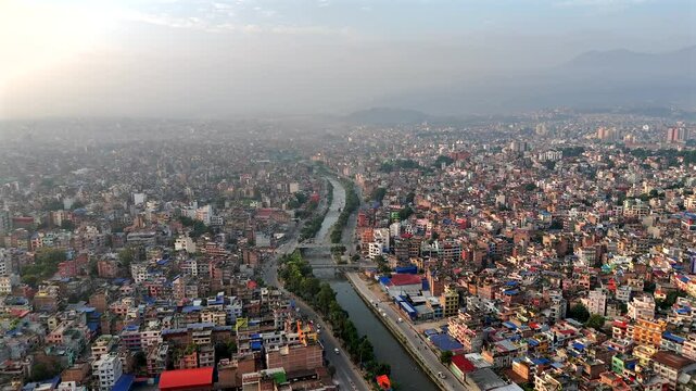 Aerial view of a river winding through the city of Kathmandu, Nepal. Drone clip moving forward and right of the city during daytime with a haze in the sky.