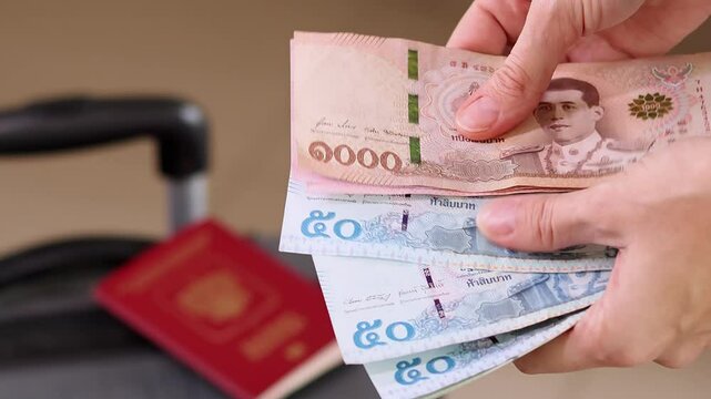 Close up of a female traveler hands counting money while packing a suitcase for a holiday trip. Preparing money and luggage for travel. Close up of a woman hands counting Thai baht THB cash money.