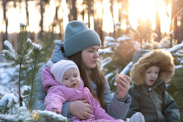 Obraz premium Mother with children eating sandwiches in a snowy forest.