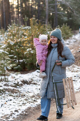 Mother walking in snowy forest with daughter in pink snowsuit and sled