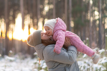 Mother lifting her little daughter in a pink jumpsuit in a snowy forest