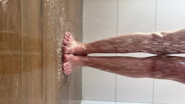 Bare feet standing under running water in the shower on a tiled bathroom floor