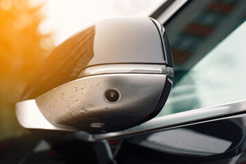 Car side mirror with an integrated camera, advanced automotive technology for safety and parking assistance. Side mirror with built-in camera on black car, safety features for enhanced visibility