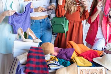 Young women choose things at flea market. Casual clothes, shoes, hats, bags, jewellery. Idea of exchange your old wardrobe for new. Eco friendly cloth concept. Zero waste shopping, reduce and reuse