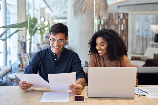Professional business team of two diverse advisors, employees man and woman, manager and client talking using laptop computer discussing documents working in office at work meeting.