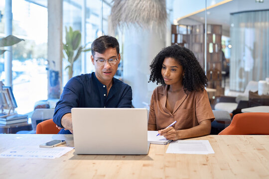 Busy team professional employees working together on computer discussing online technology data at work. Two young diverse coworkers business people using laptop and talking at office meeting.
