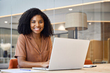 Portrait of happy young African American business woman employee using laptop computer at work in...