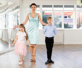 Fototapeta premium Smiling small dance partners, preteen girl and boy with female teacher in elegant outfit gracefully bowing in bright choreography studio, concluding successful performance....