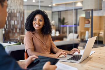 African American bank manager consulting client at meeting. Diverse professional employees using laptop discussing document in office. Business team two people man and woman talking working together.