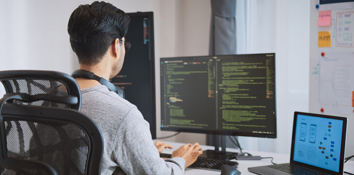 Young adult Asian male software developer coding program on desktop computer. Man work from home, remote working, freelance programmer job, smart digital nomad lifestyle concept