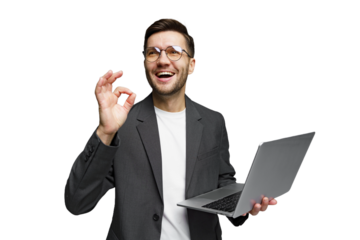 Smiling man in a suit holds a laptop while signaling approval in a bright setting