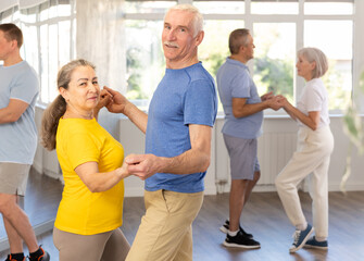 Couple of elderly man and elderly woman dancing waltz in studio