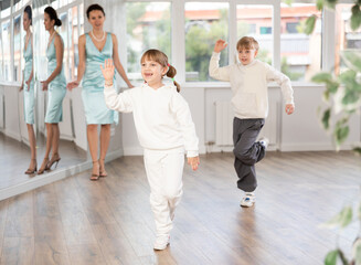 Smiling preteen girl practicing vigorous jitterbug moves with boy partner during dance lesson in...