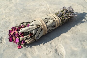 Smudge stick, crafted with dried lavender, sage, and rose petals, bound with twine, lies on a textured stone surface