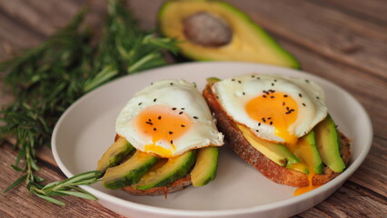 Healthy breakfast for two, couple. Spreading Yolk Two Toasts avocado fried egg, rosemary. 4K Preparing toast breakfast with avocado slices rye wholegrain bread and sunny side up egg on top