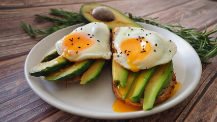 Yolk Two Toasts with avocado fried egg, rosemary. Preparing healthy avocado toast for breakfast with avocado slices rye wholegrain bread and sunny side up egg on top. Healthy breakfast for two, couple
