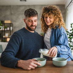 happy couple prepare oatmeal with milk for breakfast together at home