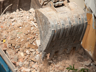 Excavator removing debris from a demolition site and dumping it into the back of a truck