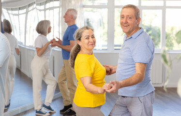 Group of elderly pensioners learn to dance a couple tango dance in a dance class