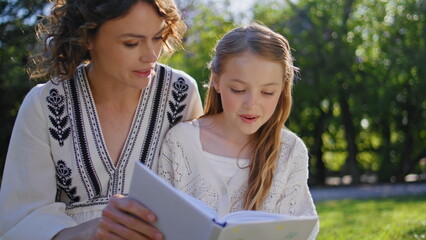 Fototapeta premium Woman parent daughter reading book sitting nature closeup. Mother kid resting