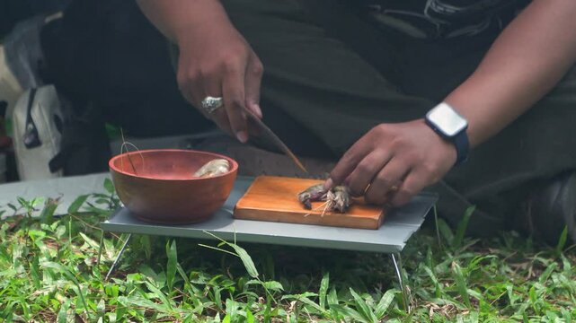 Close up of the activity of an Asian male adventurer cooking grilled shrimp using charcoal and wood. The bushcraft concept makes grilled shrimp with simple equipment in the lush wilderness