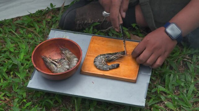 Close up of the activity of an Asian male adventurer cooking grilled shrimp using charcoal and wood. The bushcraft concept makes grilled shrimp with simple equipment in the lush wilderness