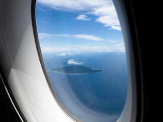 Fototapeta premium View through airplane window, porthole of an airplane that flying above the clouds and coast of one of Seychelles island La Digue