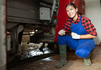 Young female farmer working with automatic milking machine on farm