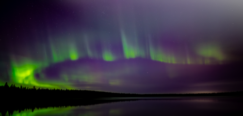 Bright green and purple Aurora reflecting in calm lake with partly transparent sky
