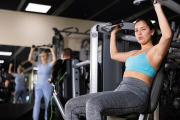Active young woman training at overhead press machine in gym