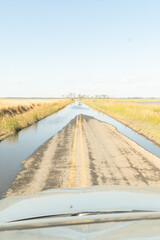 Vertical view of a remote American farm road with excess rain and sea water collecting upon the double yellow lined asphalt due to rising ocean levels combined with land erosion 