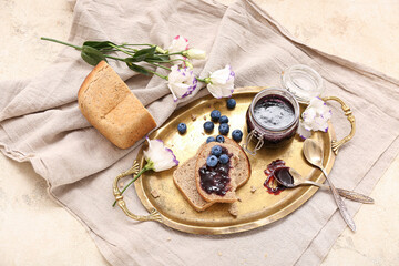 Tray with bread pieces, jar of blueberry jam and flowers on table, closeup