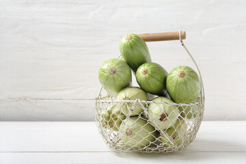 Basket with fresh green zucchini on white wooden background