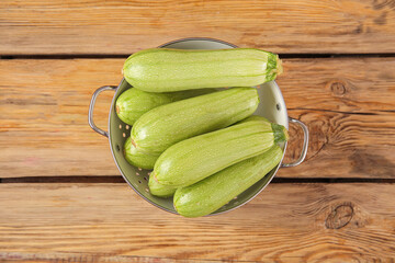 Colander with fresh green zucchini on wooden background