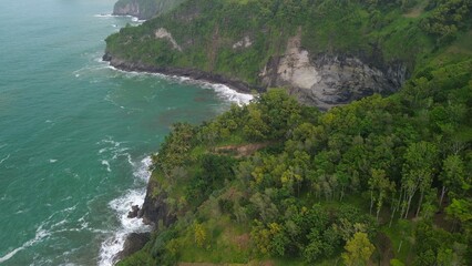 Aerial drone view of coastline with hills and trees, as well as view of coral cliffs and sea with waves from the ocean in Sagara view also known as Karang Bolong Beach Kebumen Central Java Indonesia