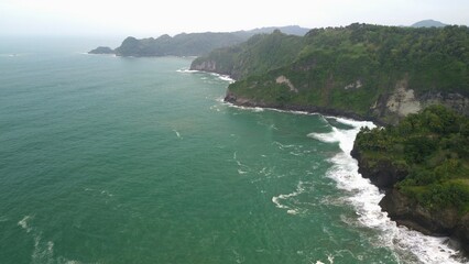 Aerial drone view of coastline with hills and trees, as well as view of coral cliffs and sea with waves from the ocean in Sagara view also known as Karang Bolong Beach Kebumen Central Java Indonesia