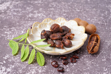Plate of tasty tamarinds, seeds and leaf on grey background