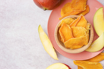 Wooden bowl with slices of dried mango and fresh fruit on white table