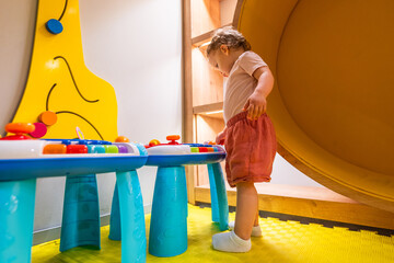 Young girl exploring buttons and shapes at activity table in colorful daycare playroom