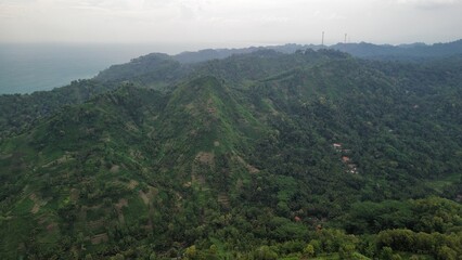 Naklejka premium Drone view of Embung Srati or Embung Silayur Kebumen, a large water reservoir on green hills with forests and trees and rows of hills around it.