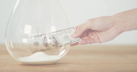 Image of hand holding banknote over hourglass