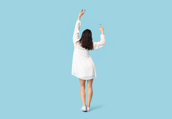 Young woman in stylish white dress dancing on blue background, back view