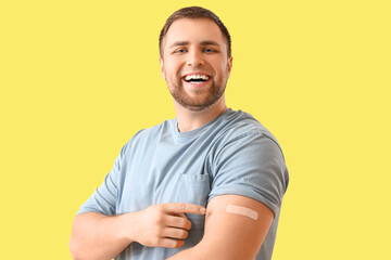 Young man with applied medical patch on yellow background. Vaccination concept