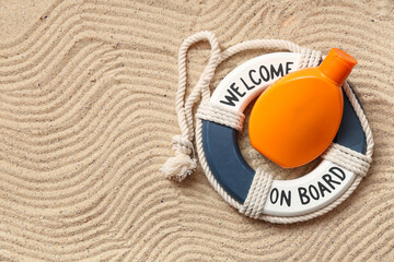 Bottle of sunscreen cream and decorative lifebuoy on sand