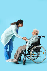 Obraz premium Young African-American female medical worker with elderly woman on wheelchair against blue background