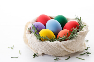 Colorful Easter eggs in a basket on white wooden table.