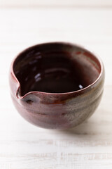 Japanese tea bowl glazed with red color on white wooden table.