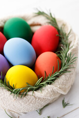 Colorful Easter eggs in a basket on white wooden table.